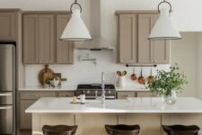 a super stylish modern farmhouse kitchen done in taupe and white, with shaker cabinets, white stone countertops and white subway tiles, white pendant lamps and dark stools