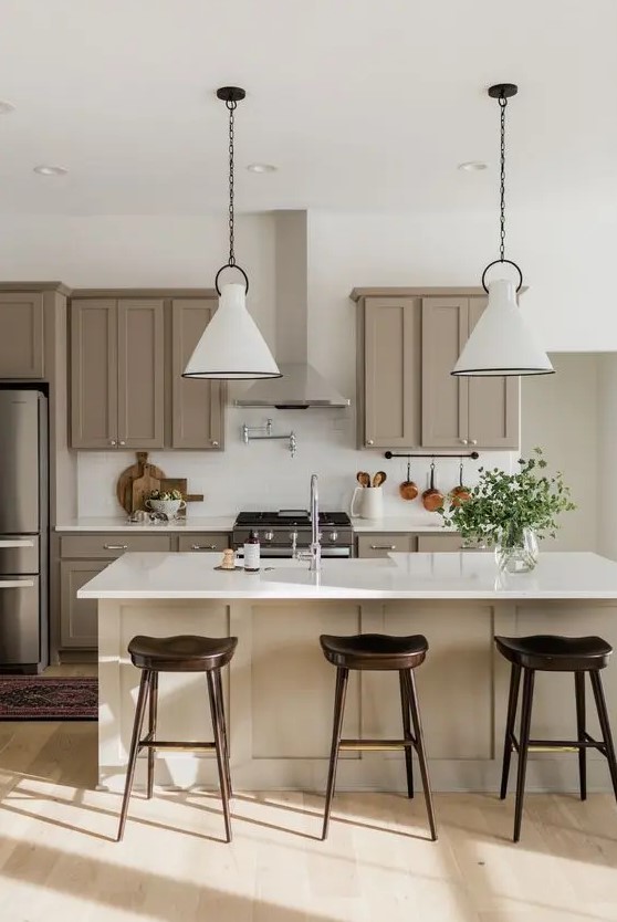 a super stylish modern farmhouse kitchen done in taupe and white, with shaker cabinets, white stone countertops and white subway tiles, white pendant lamps and dark stools