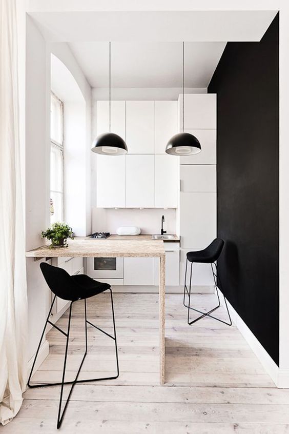a tiny yet super chic black and white kitchen with sleek cabinetry, a bar countertop and black stools and pendant lamps