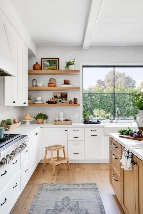 a welcoming white L-shaped kitchen in farmhouse style with light-stained wooden items and a large window