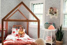 a whimsy girl’s room with spotted wallpaper, a house-shaped bed with bright bedding, a white nightstand, a basket with pillows