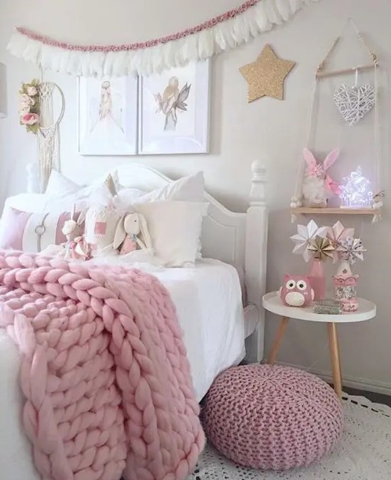 a white bedroom with vintage and modern white furniture, pink blankets and a pouf, a tassel garland and pink toys