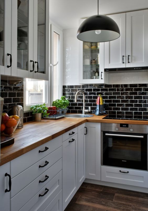 a white farmhouse kitchen with a black glazed tiles, butcherblock countertops, black pendant lamps