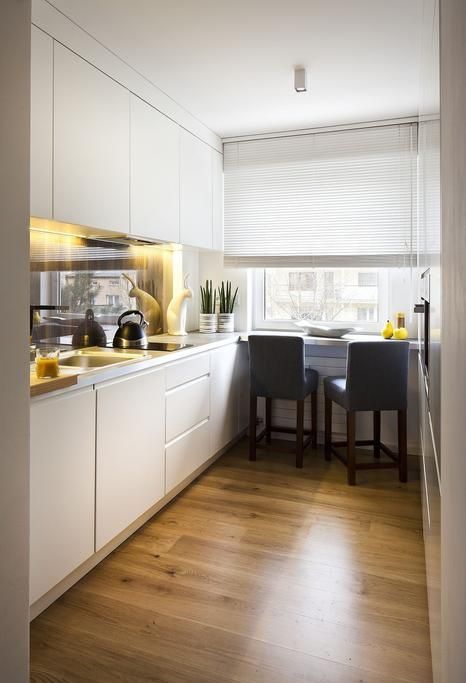a white minimalist kitchen with a glossy backsplash, built-in lights, a windowsill breakfats bar