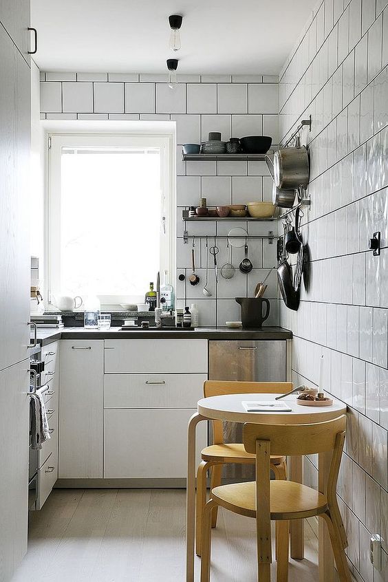 a white modern kitchen completely clad with tiles, black countertops, a round table and stools is comfy