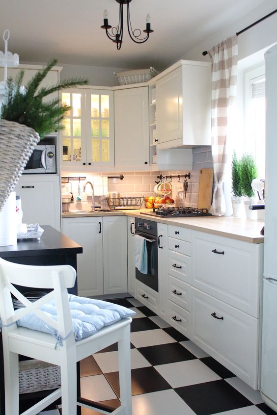 a white rustic kitchen with a checked floor, butcherblock countertops and tall stools and vintage chandeliers