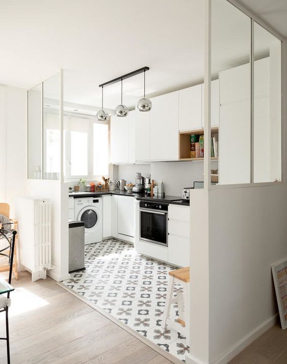 a white sleek kitchen with a white backsplash, black coutnertops and metallic lamps plus a printed tiled floor