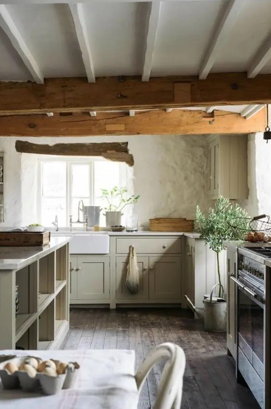an English cottage kitchen with wooden beams, light green cabinets, rough walls and a large kitchen island