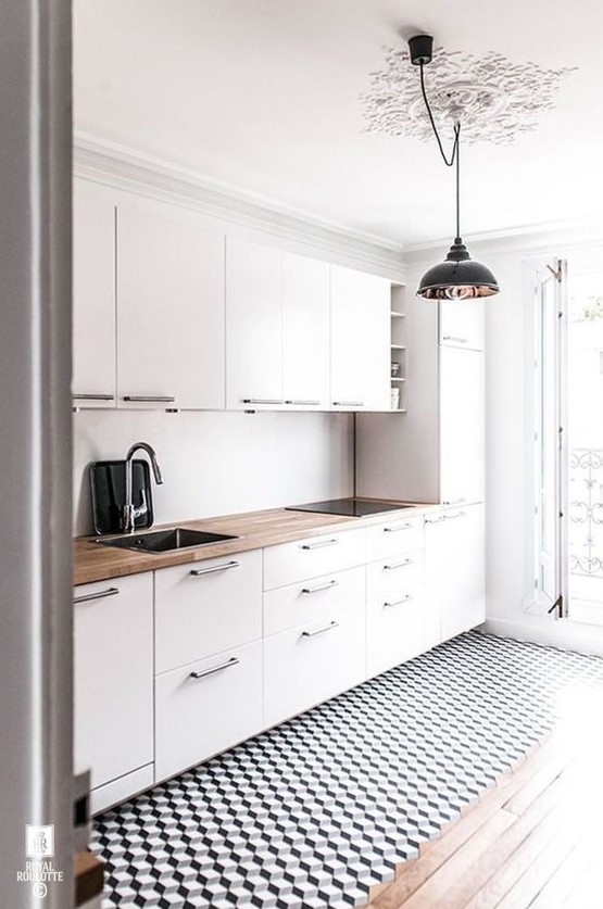 an airy Scandinavian kitchen with white cabinets, butcherblock countertops, a geometric floor and pendant lamps