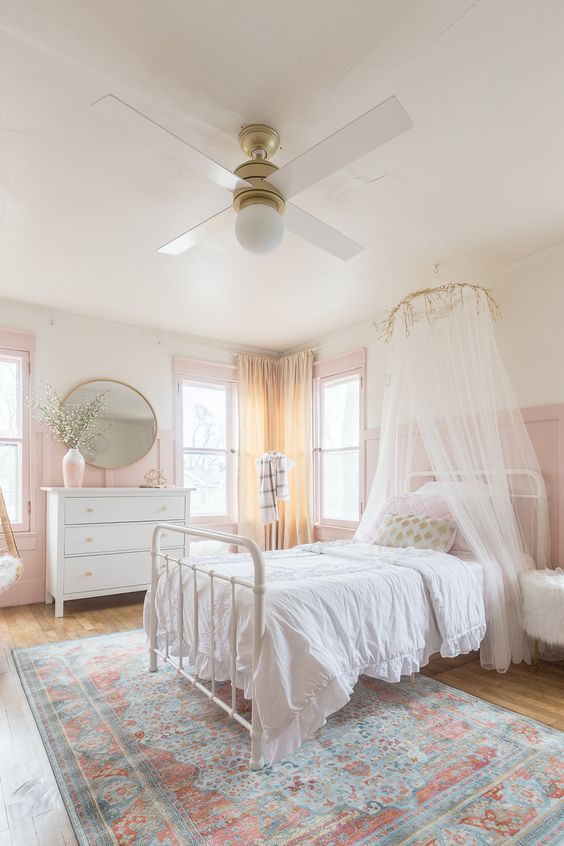 an airy girl's bedroom with pink paneling, a white bed with neutral bedding and a canopy, a white dresser