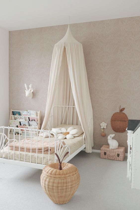 an amazing girl's room with a blush printed accent wall, a white bed with a canopy, an apple-shaped basket and a stand with books