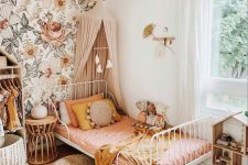 an earthy-tone girl’s bedroom with floral wallpaper, a white metal bed with pink bedding, a canopy, an open wardrobe and a play house