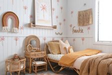 an earthy-tone girl’s room with paneling, rattan furniutre, warm-colored bedding, a printed rug, fringe and some hangings on the wall
