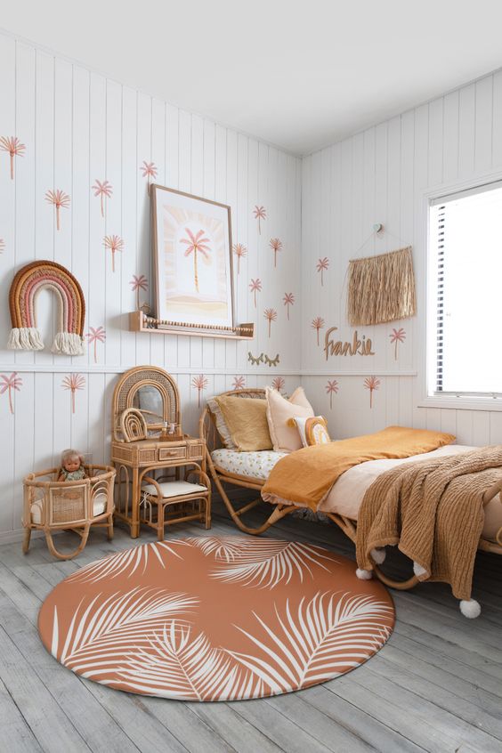 an earthy-tone girl's room with paneling, rattan furniutre, warm-colored bedding, a printed rug, fringe and some hangings on the wall