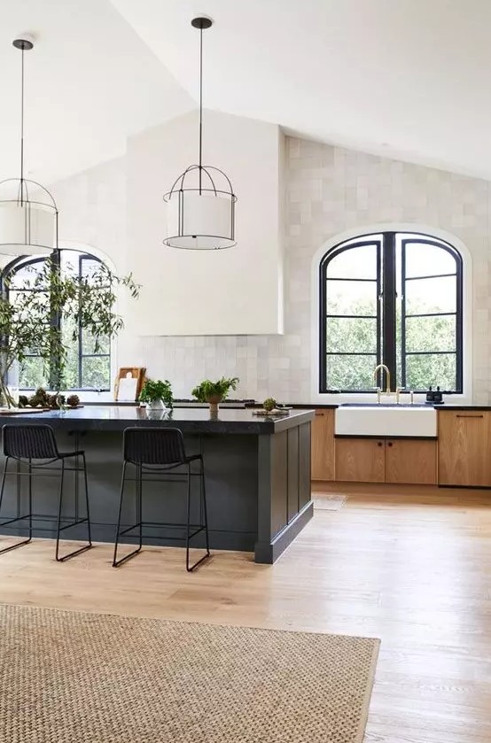 an elegant vintage kitchen with stained cabinets, a black kitchen island, a white hood and arched window with black frames