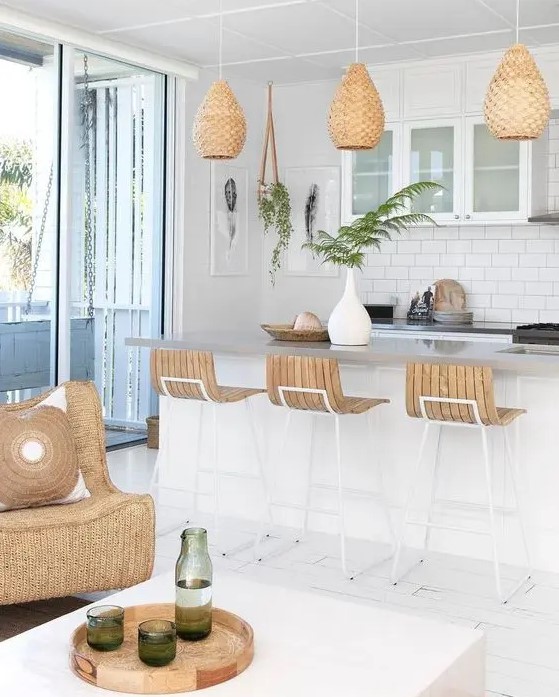 an inspiring beach kitchen with white cabinets, a kitchen island, woven pendant lamps, wooden sotols, a wicker chair and a matching tray