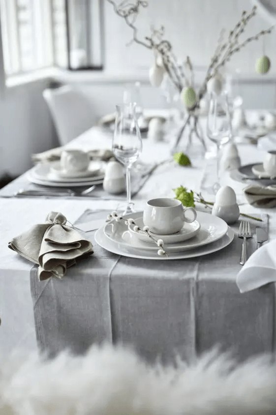 a Scandinavian Easter table setting with grey and white linens, chic porcelain, willow and greenery plus lots of eggs