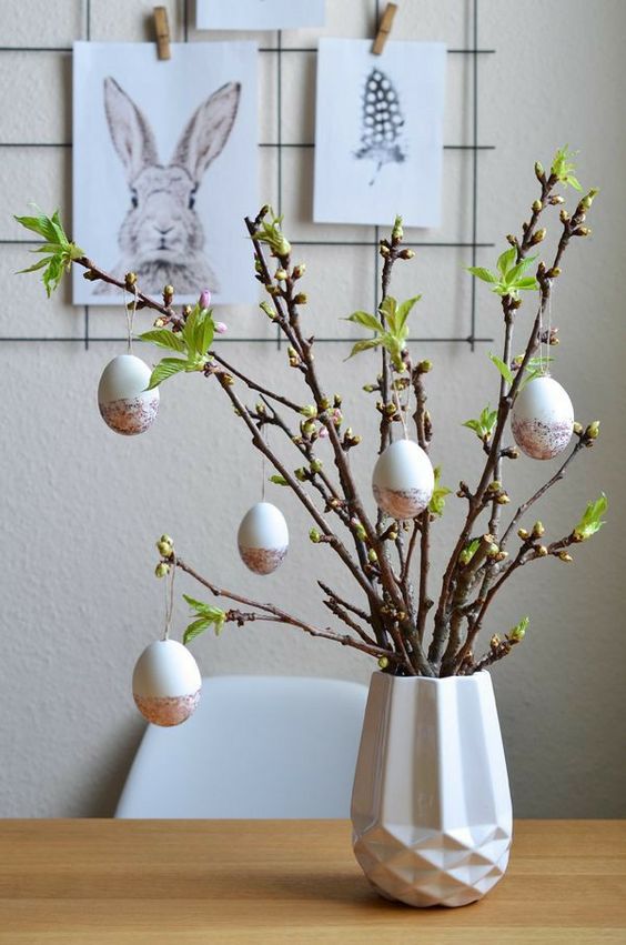 a beautiful Easter centerpiece of a faceted vase with greenery branches and color block eggs as decor is a cool idea