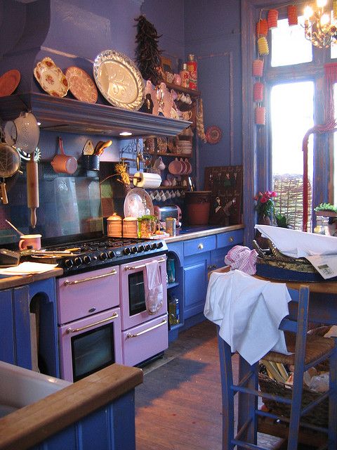 a bold retro kitchen with purple cabinets, pink appliances, gold handles and open shelves with pretty objects on display is wow