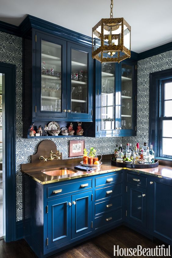 a bright blue kitchen with blue printed wallpaper, bold stained countertops and a backsplash plus gold touches here and there