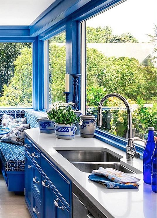 a bright blue kitchen with bold walls and cabinetry, white countertops and patterned blue and white plants