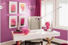 a bright home office with a purple accent wall, an elegant white desk, a grey chair, a fuchsia sofa and a pink and copper burst chandelier