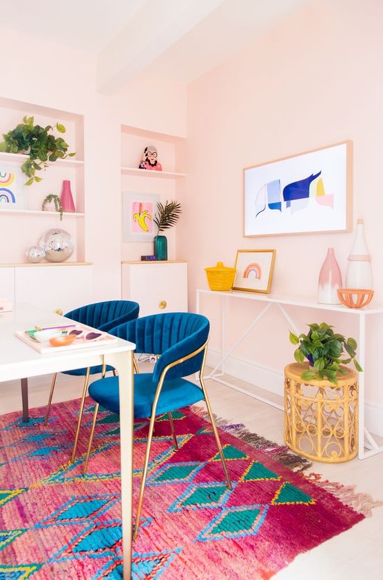 a bright home office with light pink walls, navy chairs, a colorful gallery wall and a rug, potted greenery