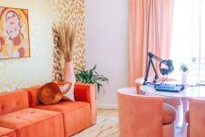 a bright maximalist home office with a gold stencild wall, a desk for several people, pink chairs, a coral sectional and bold rugs