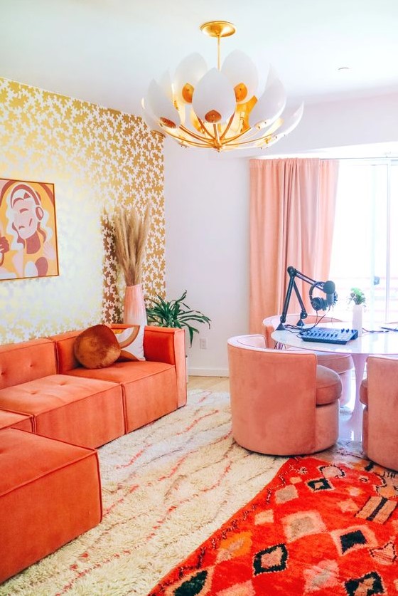 a bright maximalist home office with a gold stencild wall, a desk for several people, pink chairs, a coral sectional and bold rugs