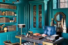 a bright maximalist home office with teal walls and matching built-in furniture and shelves, a refined desk, a navy and leather chairs, a chic chandelier