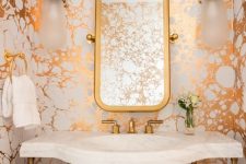 a bright powder room with metallic marble wallpaper, brass touches and a white stone sink