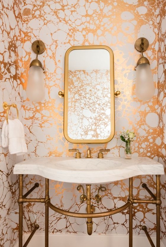a bright powder room with metallic marble wallpaper, brass touches and a white stone sink