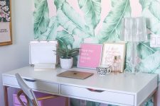 a bright tropical home office nook with a tropical leaf wall, a pink storage unit and art and touches of gold and brass