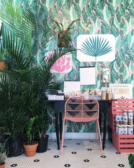 a bright tropical home office with tropical wallpaper, bright artworks and potted plants, a vintage desk and pink furniture