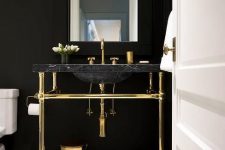 a chic powder room with black walls, a black marble sink, gold fixtures and legs plus a mosaic tile floor