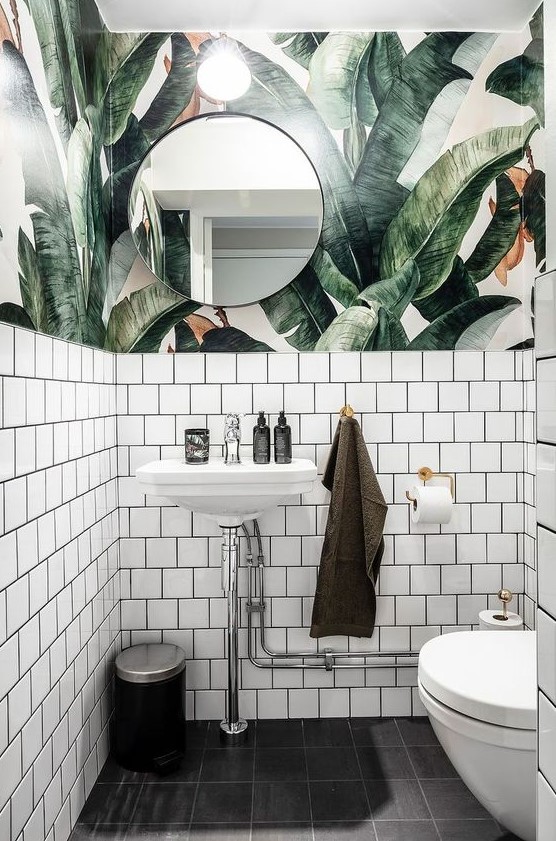 a chic powder room with tropical leaf wallpaper, white tiles and neutral metallics feels tropical