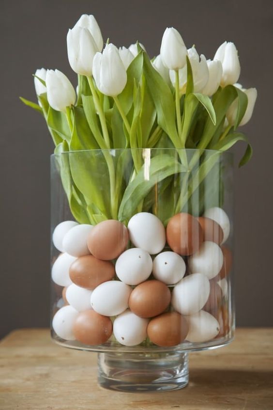 a classy modern Easter centerpiece of a clear glass with faux eggs and white tulips is a very natural and fast to make arrangement
