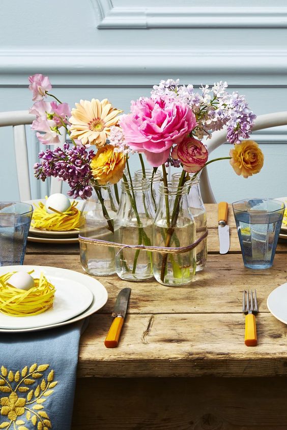 a classy spring centerpiece of glass bottles with yellow, pink and lilac blooms is a stylish idea for a rustic tablescape