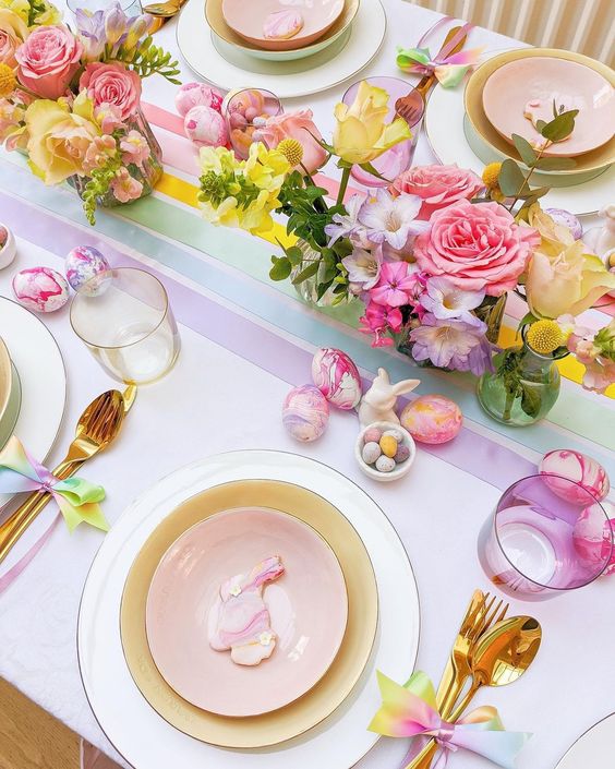 a colorful Easter tablescape with bright blooms, pastel plates, colorful glasses, gold cutlery and bright marble eggs