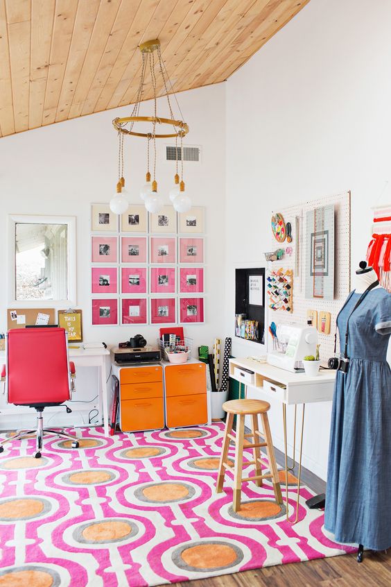 a colorful home office with a bold printed rug, a red leather chair, orange storage cabinets, an ombre pink gallery wall is a lovely space to be in