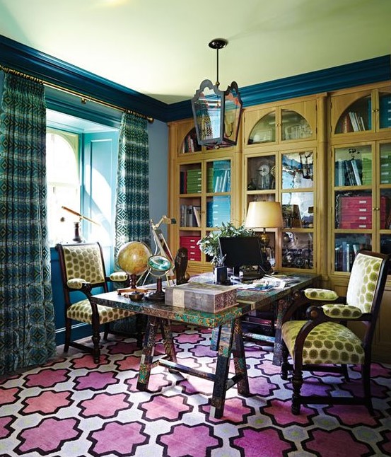 a colorful home office with blue walls, yellow built in bookcases, a colorful trestle desk and a colorful rug, bold mustard chairs
