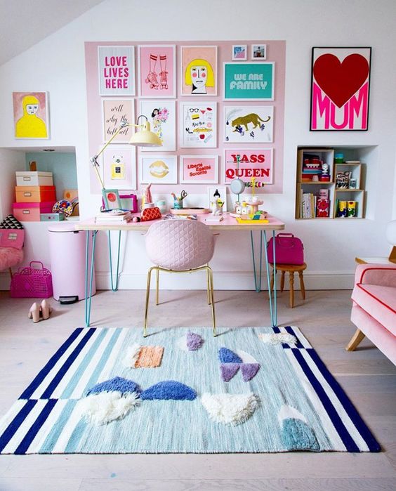 a colorful home working space with a blue fringe rug, a pink desk and a pink chair, a pink litter bin and a pink accent wall with colorful artwork is pure fun
