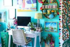 a colorful maximalist home office with a turquoise accent wall, a white desk, a green cabinet and lots of artworks and textiles in bold shades