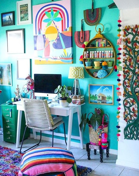 a colorful maximalist home office with a turquoise accent wall, a white desk, a green cabinet and lots of artworks and textiles in bold shades