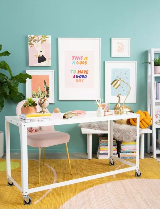 a colorful working space with turquoise walls, a blush chair, a white desk, a colorful rug and a bright gallery wall