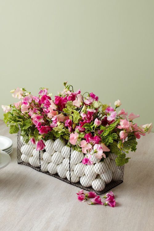a cool Easter centerpiece of a wire box with eggs, pink blooms and greenery is amazing