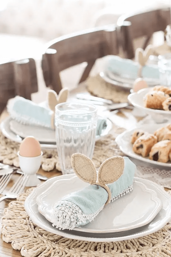 a cute Easter tablescape with woven placemats, blue napkins with bunny ears, eggs and chic glasses