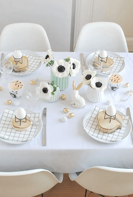 a cute and simple Easter tablescape with printed napkins, wood slices with eggs on stands, white blooms, bunnies and faux mini eggs