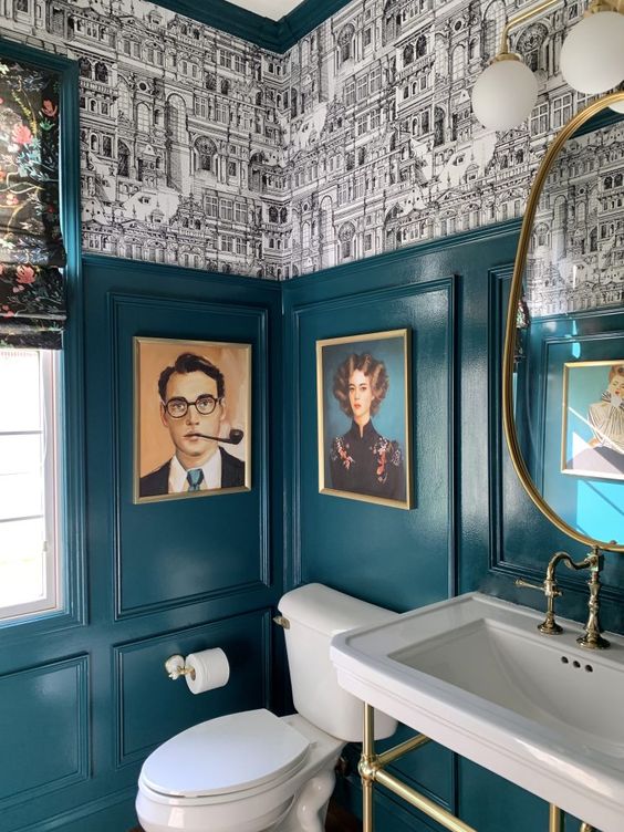 a dramatic powder room with teal paneling, bold wallpaper, artwork, white appliances and a mirror of a very catchy shape
