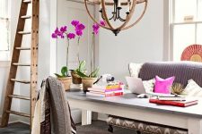 a fancy and whimsy home office with a grey sofa and woven chair, a large desk, a sphere chandelier, a ladder and colorful touches